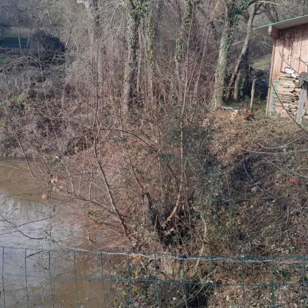 Paysage rural en hiver près d’un ruisseau boueux, bâtiment en bois et clôture métallique, travaux sola à limoux